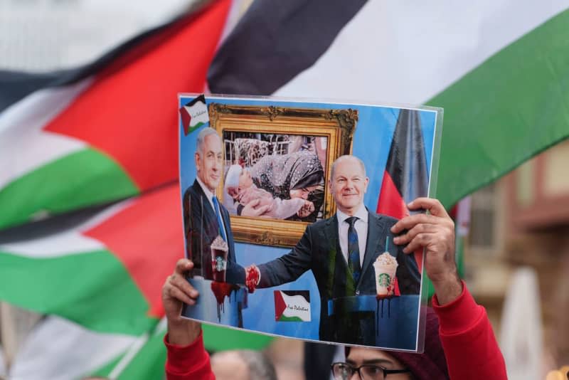 A rally participant holds a poster showing Benjamin Netanyahu, Israeli Prime Minister, and Olaf Scholz, German Chancellor, demonstrating against the conflict in Gaza during the Easter marches in Hesse. Andreas Arnold/dpa